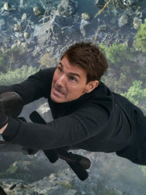 Szene aus Mission Impossible 7: Tom Cruise hängt weit über dem Boden nur mit einer Hand an einem Hubschrauber