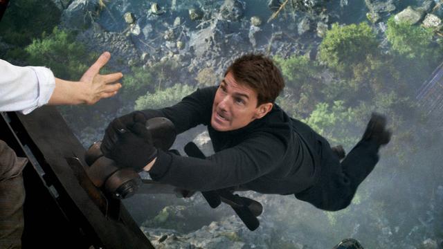 Szene aus Mission Impossible 7: Tom Cruise hängt weit über dem Boden nur mit einer Hand an einem Hubschrauber