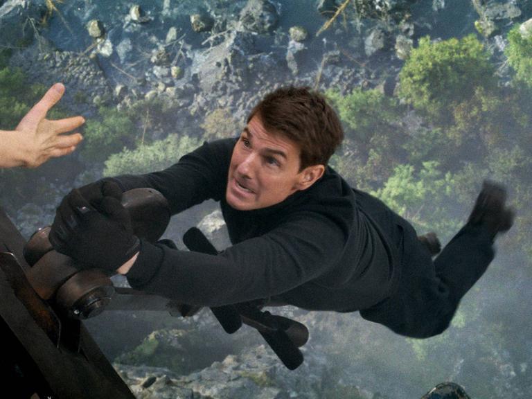 Szene aus Mission Impossible 7: Tom Cruise hängt weit über dem Boden nur mit einer Hand an einem Hubschrauber