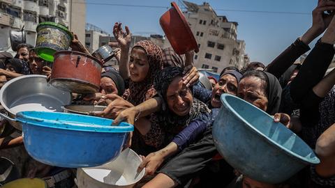 Frauen, Männer und Kinder in Gaza-Stadt strecken Helfer, die Lebensmittel verteilen, bunte Plastikschüsseln entgegen.