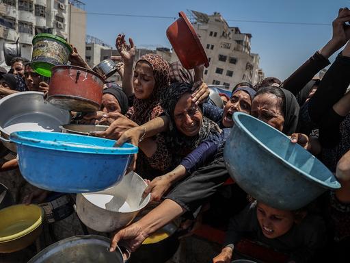 Frauen, Männer und Kinder in Gaza-Stadt strecken Helfer, die Lebensmittel verteilen, bunte Plastikschüsseln entgegen.