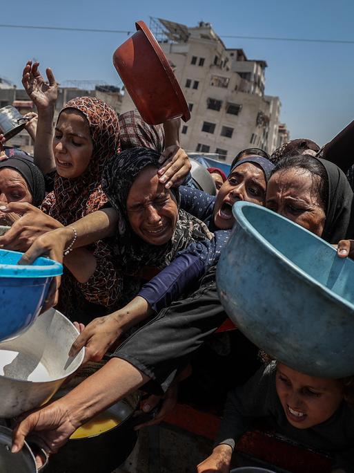 Frauen, Männer und Kinder in Gaza-Stadt strecken Helfer, die Lebensmittel verteilen, bunte Plastikschüsseln entgegen.