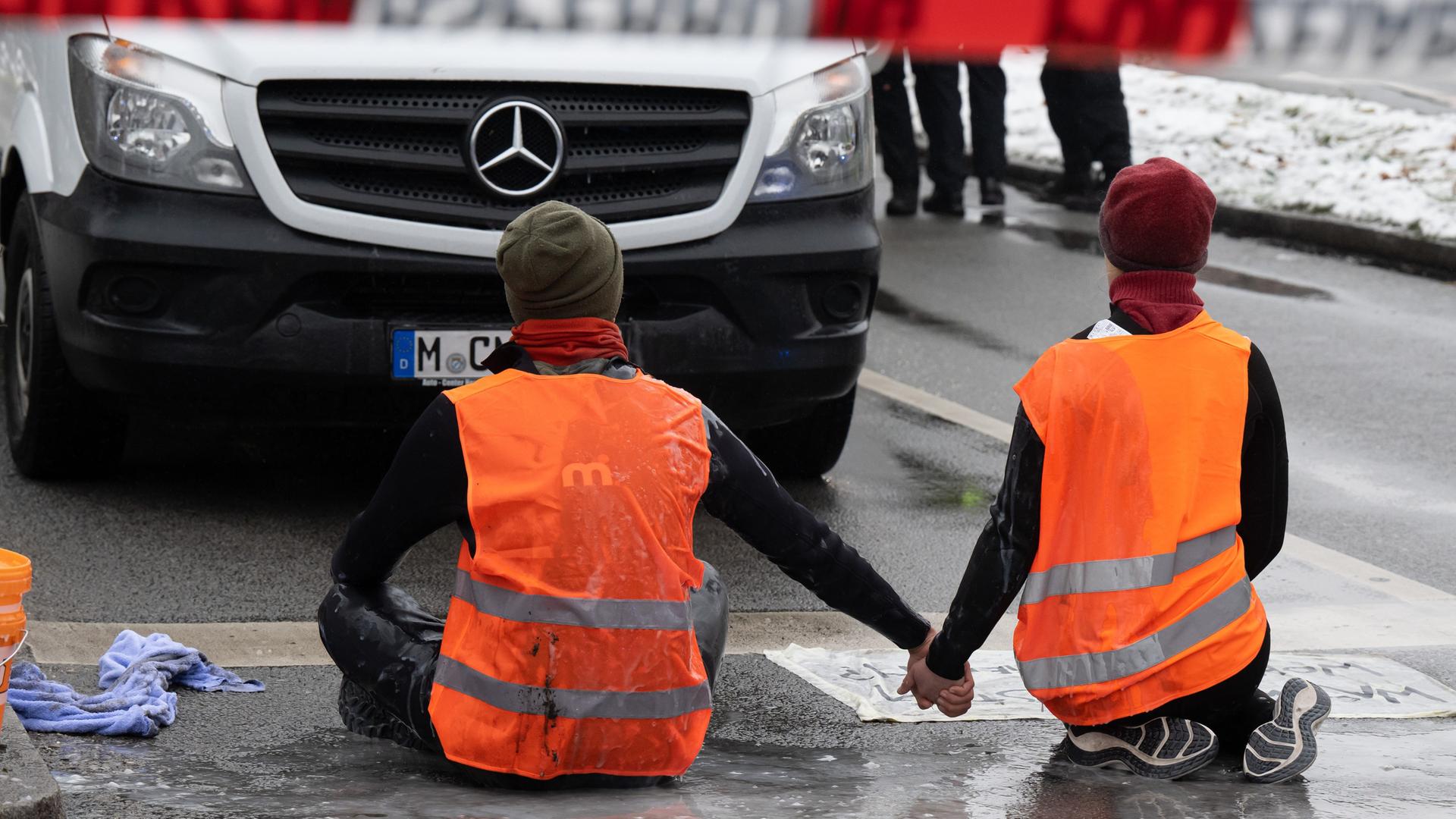Zwei Klimaaktivisten versuchen sich auf einer Straße festzukleben.