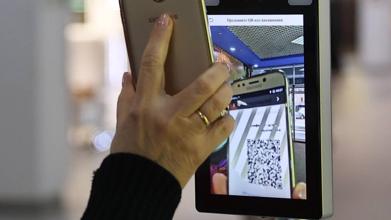 Hand mit Smartphone am Scanner: Eine Frau scannt ihren QR-Impf-Code, bevor sie eine Shoppingmall betritt.
