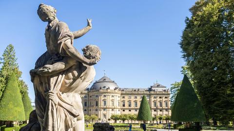 Blick auf die Rücken einiger Figuren, die sich der Residenz Würzburg zuwenden. 