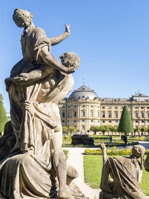 Blick auf die Rücken einiger Figuren, die sich der Residenz Würzburg zuwenden. 