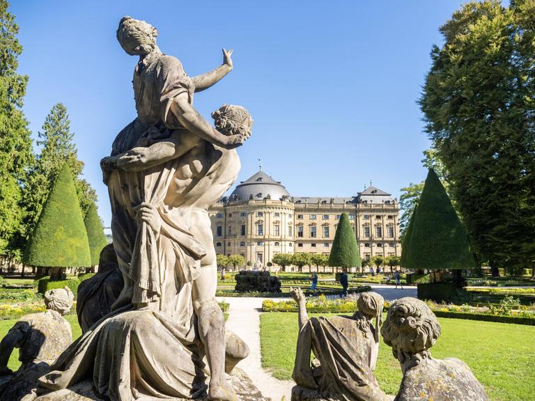 Blick auf die Rücken einiger Figuren, die sich der Residenz Würzburg zuwenden. 