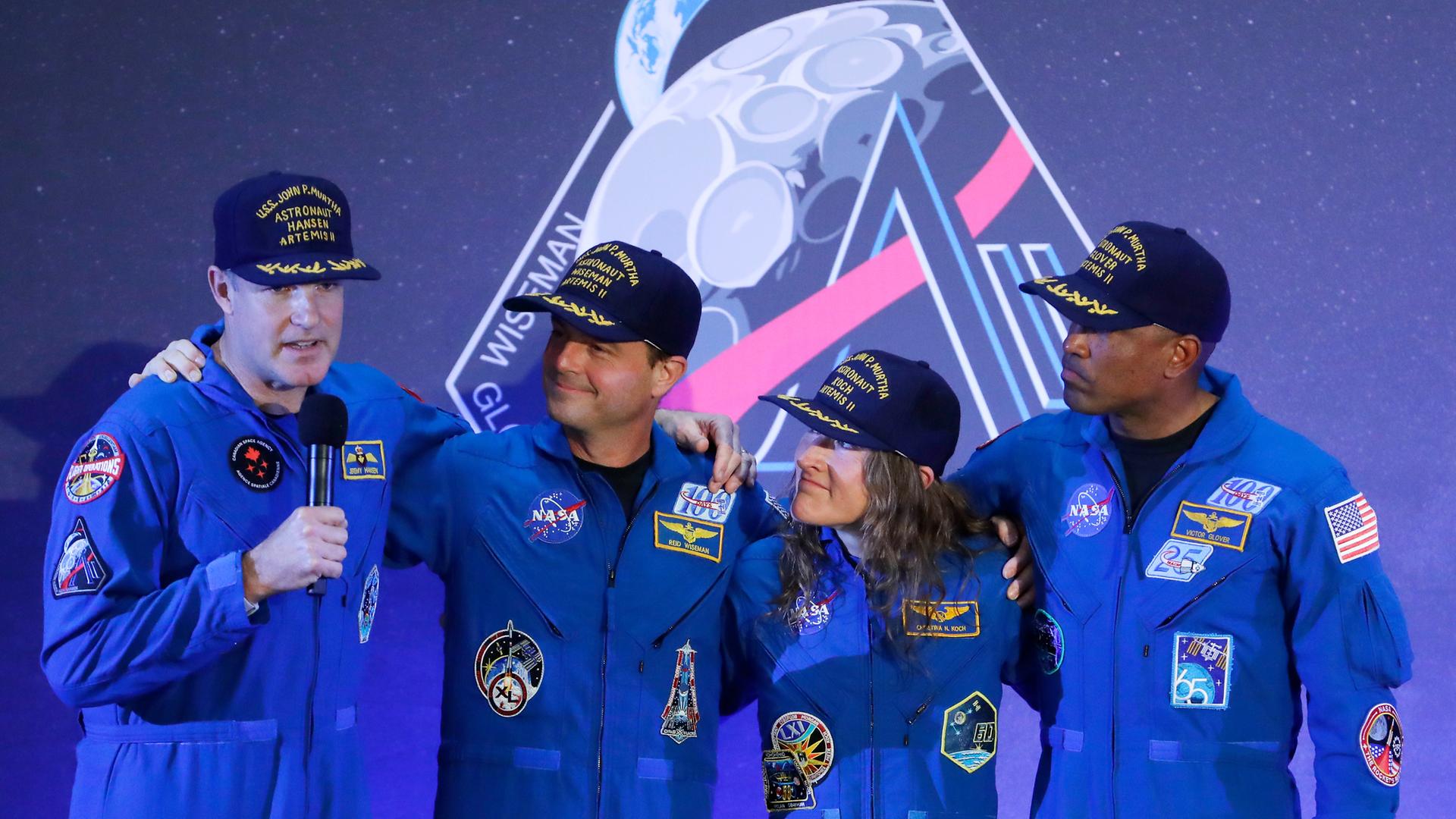 Die Besatzung der Artemis 2, drei Männer und eine Frau, steht auf einer Bühne, einer von ihnen hält ein Mikrofon in der Hand.