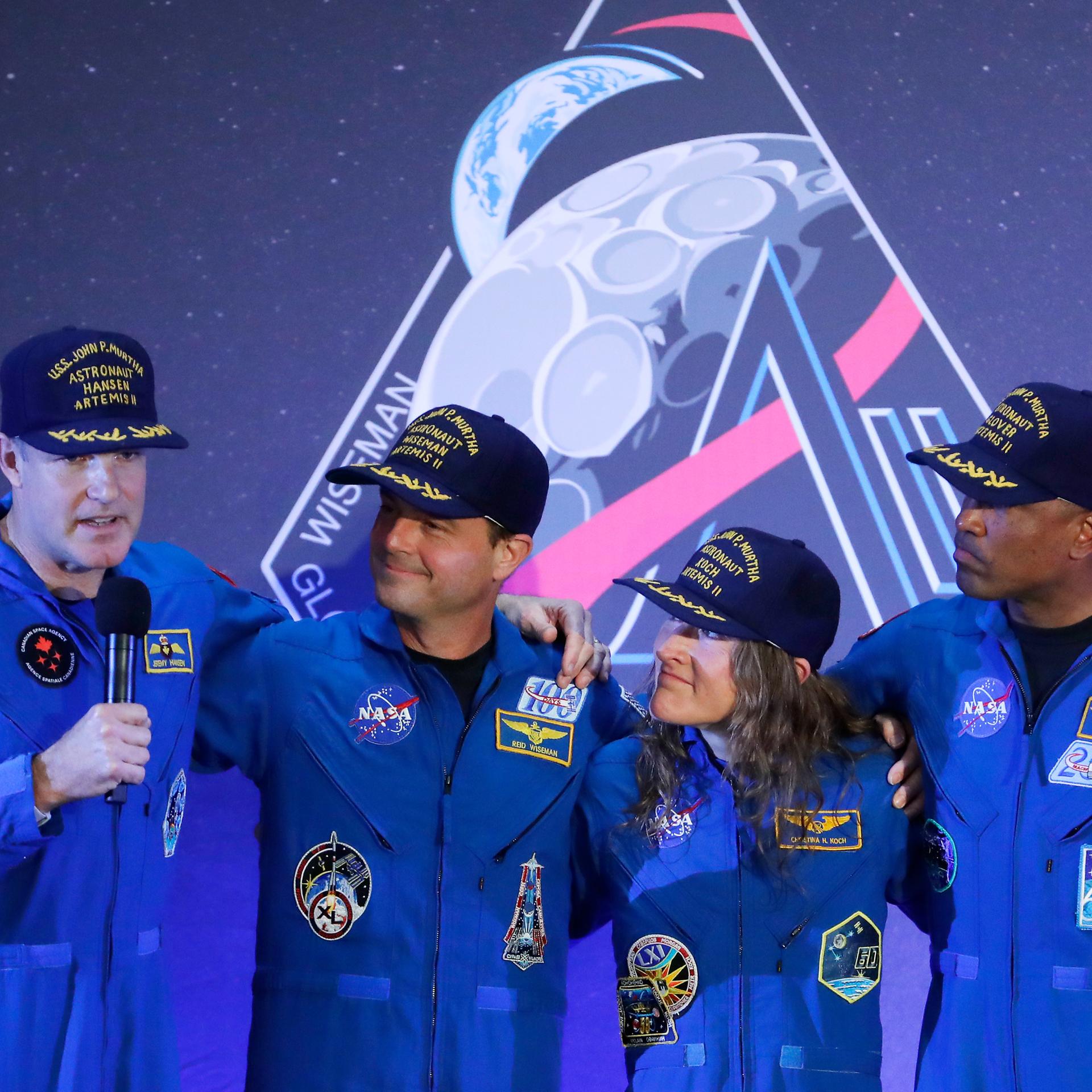 Die Besatzung der Artemis 2, drei Männer und eine Frau, steht auf einer Bühne, einer von ihnen hält ein Mikrofon in der Hand.