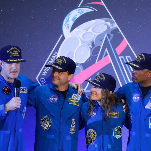 Die Besatzung der Artemis 2, drei Männer und eine Frau, steht auf einer Bühne, einer von ihnen hält ein Mikrofon in der Hand.