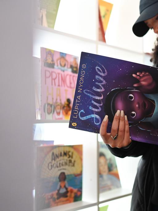 Eine Besucherin guckt sich ein Buch in der "Schwarzen Kinderbibliothek" an, in diesem Fall "Solwe" von Lupita Nyong'o.