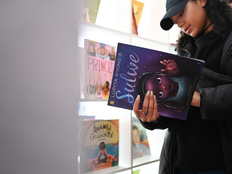Eine Besucherin guckt sich ein Buch in der "Schwarzen Kinderbibliothek" an, in diesem Fall "Solwe" von Lupita Nyong'o.