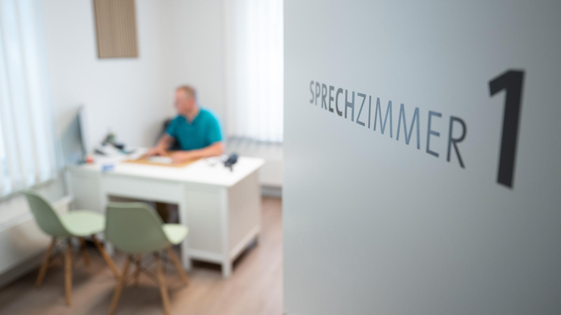 Ein Hausarzt sitzt in einem Sprechzimmer seiner Hausarztpraxis an einem Schreibtisch und arbeitet am Computer. Ein Hausarzt sitzt in einem Sprechzimmer seiner Hausarztpraxis an einem Schreibtisch und arbeitet am Computer.