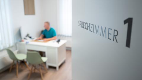 Ein Hausarzt sitzt in einem Sprechzimmer seiner Hausarztpraxis an einem Schreibtisch und arbeitet am Computer. 