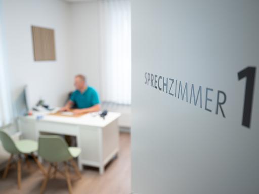 Ein Hausarzt sitzt in einem Sprechzimmer seiner Hausarztpraxis an einem Schreibtisch und arbeitet am Computer. Ein Hausarzt sitzt in einem Sprechzimmer seiner Hausarztpraxis an einem Schreibtisch und arbeitet am Computer.