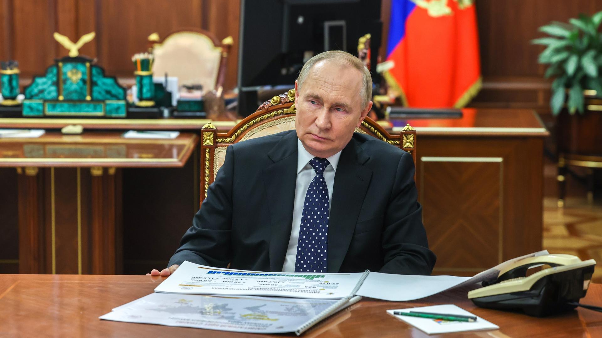 Das Bild zeigt Wladimir Putin mit ernster Miene an einem Schreibtisch mit Unterlagen.