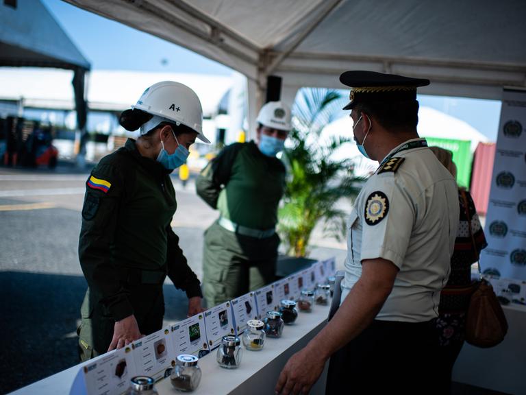 Drei Polizeibeamte treffen im Hafen von Cartagena zusammen, sie stehen vor einem Tisch, auf dem Drogen aufgebaut sind. Drei Polizeibeamte treffen im Hafen von Cartagena zusammen, sie stehen vor einem Tisch, auf dem Drogen aufgebaut sind.