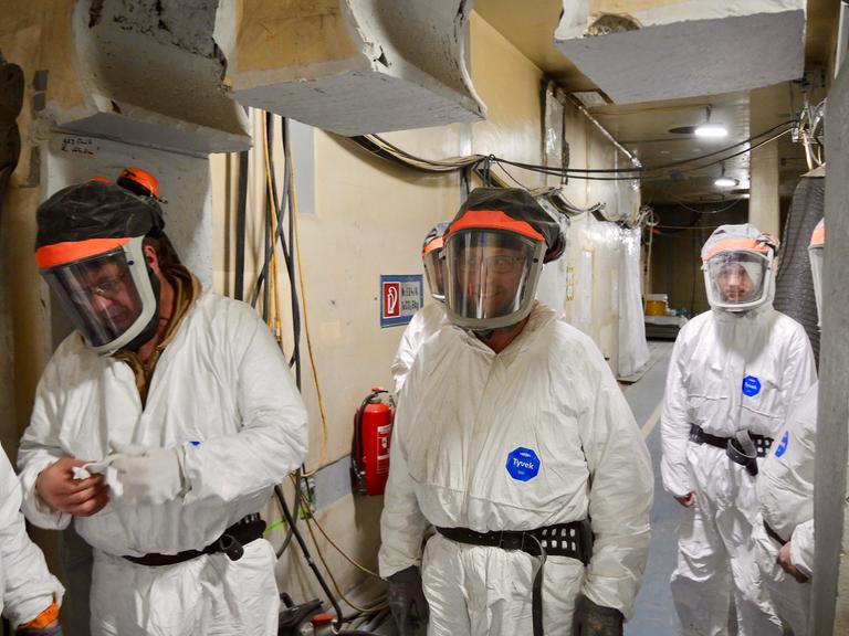 Drei Männer in weißen, strahlensicheren Schutzanzügen und Schutzbrillen gehen durch eine Halle im stillgelegten Atomkraftwerk Greifswald-Lubmin.
