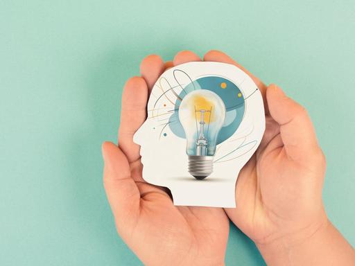 Eine Grafik: Zwei Hände halten ein aus Papier ausgeschnittenen Kopf. In dem Kopf ist eine Glühbirne. Die Grafik symbolisiert Wissenschaft und Forschung. Eine Grafik: Zwei Hände halten ein aus Papier ausgeschnittenen Kopf. In dem Kopf ist eine Glühbirne. Die Grafik symbolisiert Wissenschaft und Forschung.