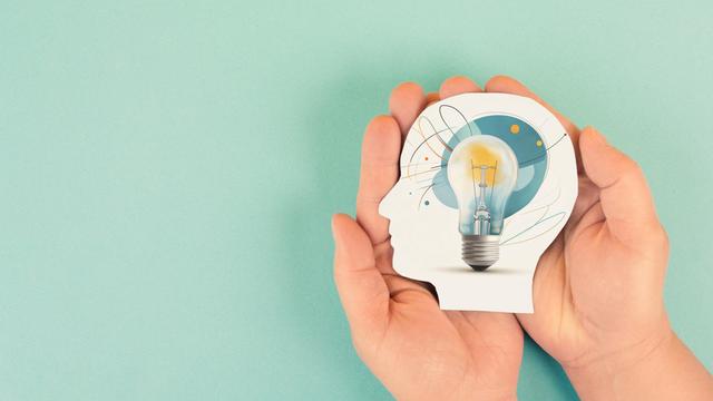 Eine Grafik: Zwei Hände halten ein aus Papier ausgeschnittenen Kopf. In dem Kopf ist eine Glühbirne. Die Grafik symbolisiert Wissenschaft und Forschung.