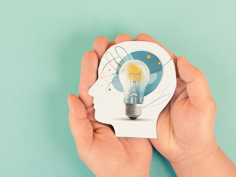 Eine Grafik: Zwei Hände halten ein aus Papier ausgeschnittenen Kopf. In dem Kopf ist eine Glühbirne. Die Grafik symbolisiert Wissenschaft und Forschung.