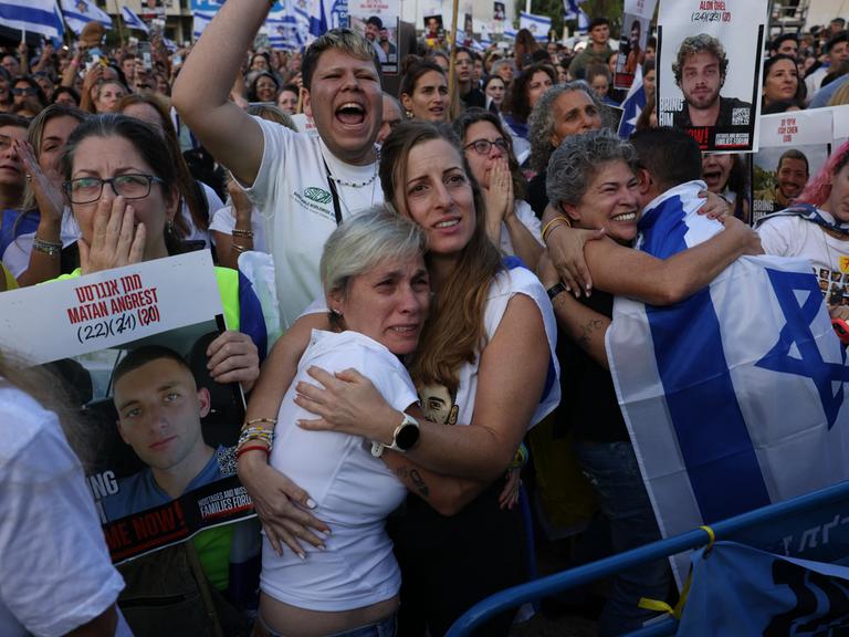 Menschen halten Israel-Flaggen in die Höhe und umarmen sich auf dem Platz der Geiseln in Tel Aviv, Israel (13.10.2025)