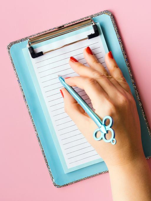 Nahaufnahme einer Hand, die mit einem Stift auf einem Notizzettel liegt.