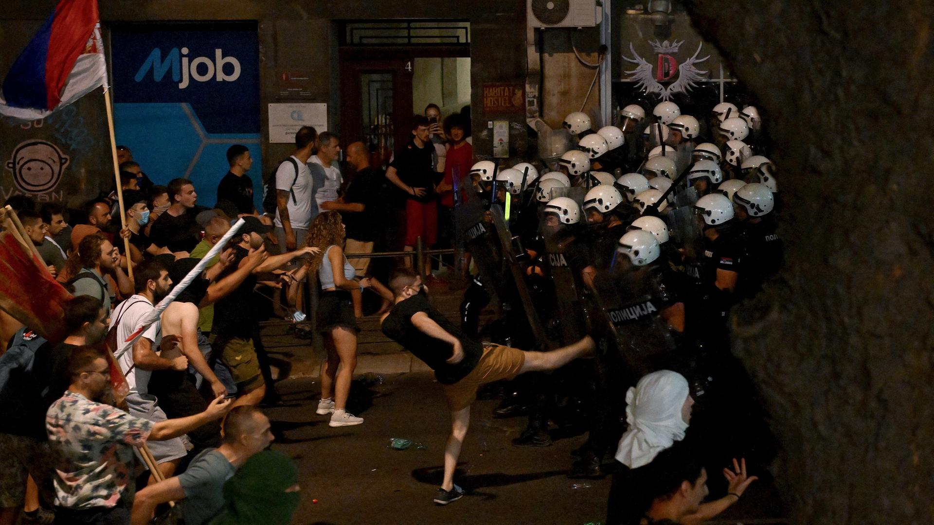 Protestierende stehen Polizisten gegenüber. Ein Demonstrant tritt einen Polizisten.