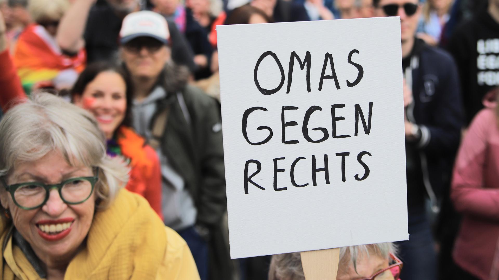 Eine Demonstrantin in einer Menschenmenge hält ein Schild mit der Aufschrift "Omas gegen Rechts" in die Höhe, sie steht zwischen Menschen auf dem Gelände der Deutzer Werft, wo am 1. Juni 2024 gegen Rechtsextremismus und Rassismus demonstrieren wird.