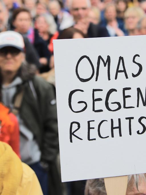 Eine Demonstrantin in einer Menschenmenge hält ein Schild mit der Aufschrift "Omas gegen Rechts" in die Höhe, sie steht zwischen Menschen auf dem Gelände der Deutzer Werft, wo am 1. Juni 2024 gegen Rechtsextremismus und Rassismus demonstrieren wird.