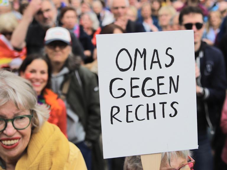 Eine Demonstrantin in einer Menschenmenge hält ein Schild mit der Aufschrift "Omas gegen Rechts" in die Höhe, sie steht zwischen Menschen auf dem Gelände der Deutzer Werft, wo am 1. Juni 2024 gegen Rechtsextremismus und Rassismus demonstrieren wird.