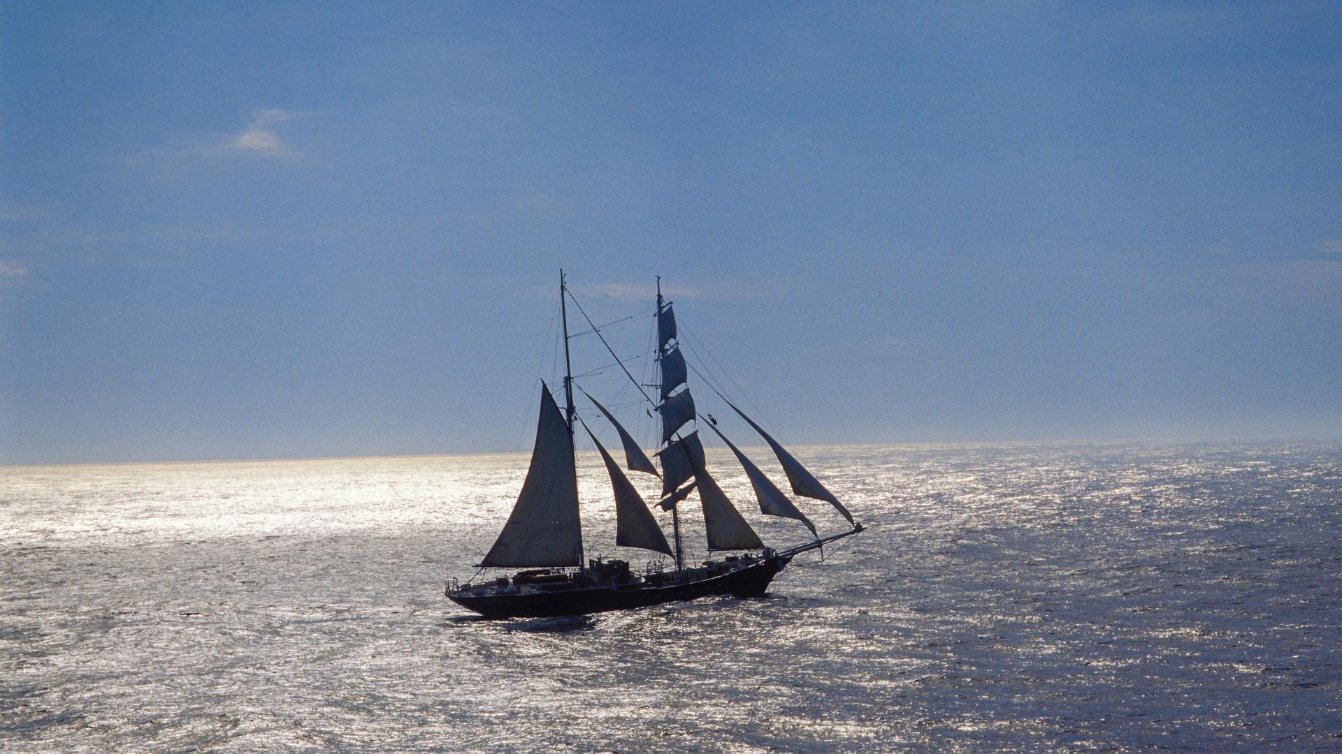 Segelschiff mit mehreren Masten am offenen Meer. Das Meer glänzt im Sonnenlicht.