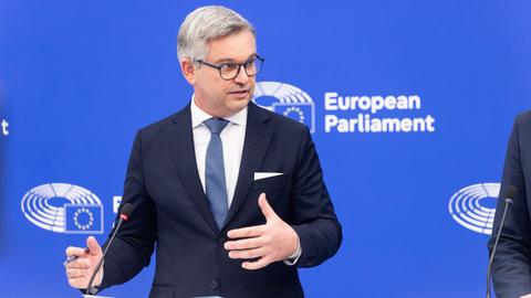  Brunner bei einem öffentlichen Auftritt im Europäischen Parlaments. Er spricht in ein Mikrofon und macht mit seinen Händen eine Geste.