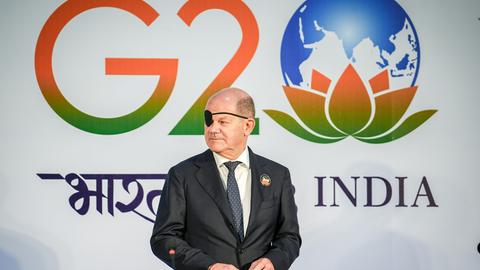 Bundeskanzler Olaf Scholz (SPD) steht mit Augenklappe vor dem Logo des G20-Gipfels in Neu Delhi in Indien.