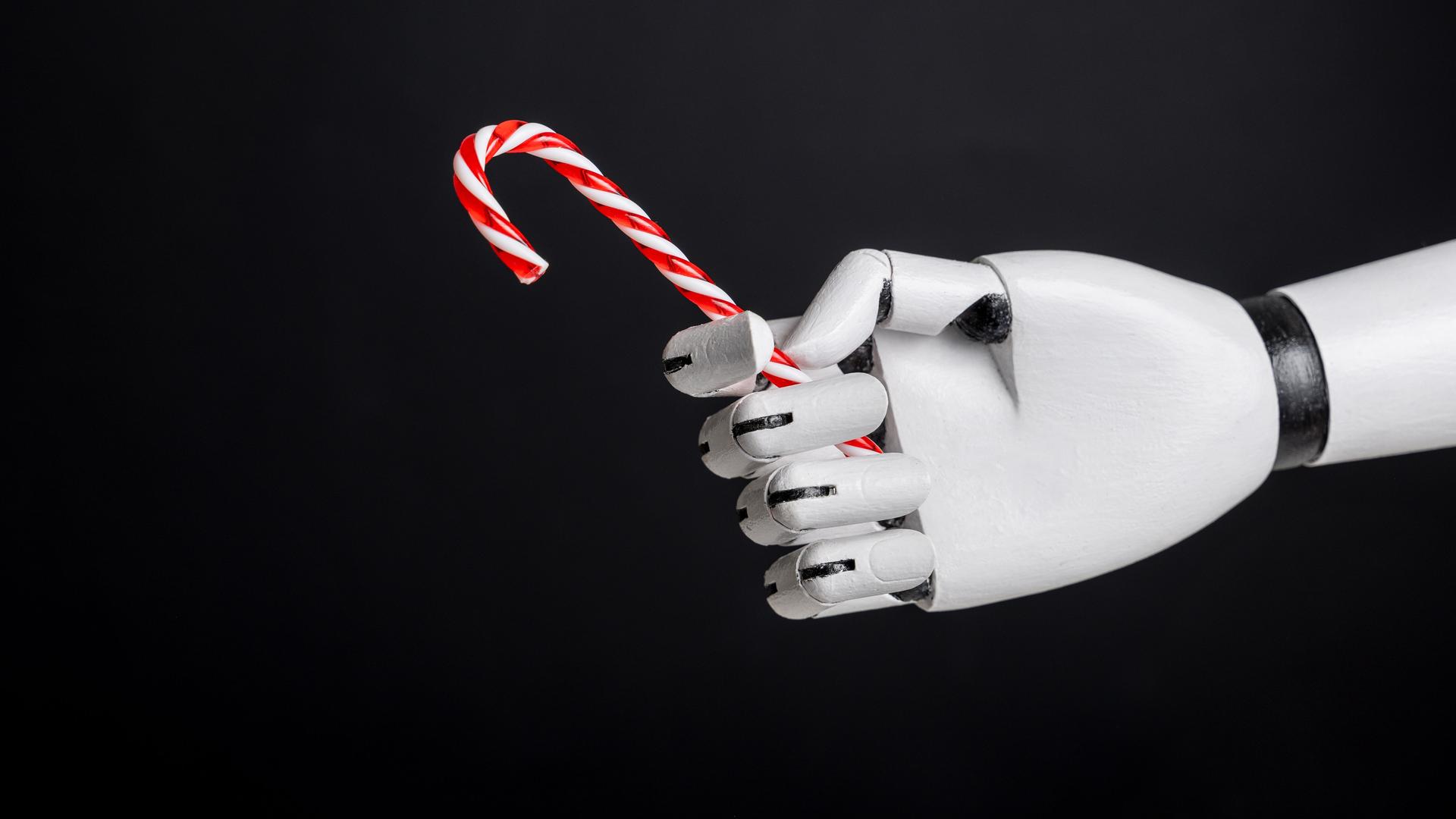 Eine Roboterhand hält Zuckerstange vor schwarzem Hintergrund. Eine Roboterhand hält Zuckerstange vor schwarzem Hintergrund.