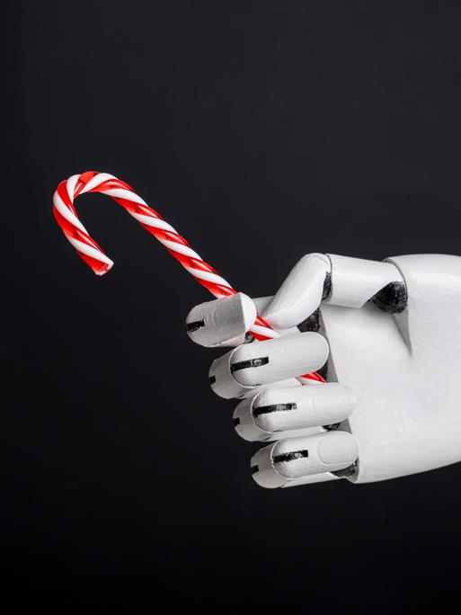 Eine Roboterhand hält Zuckerstange vor schwarzem Hintergrund. 