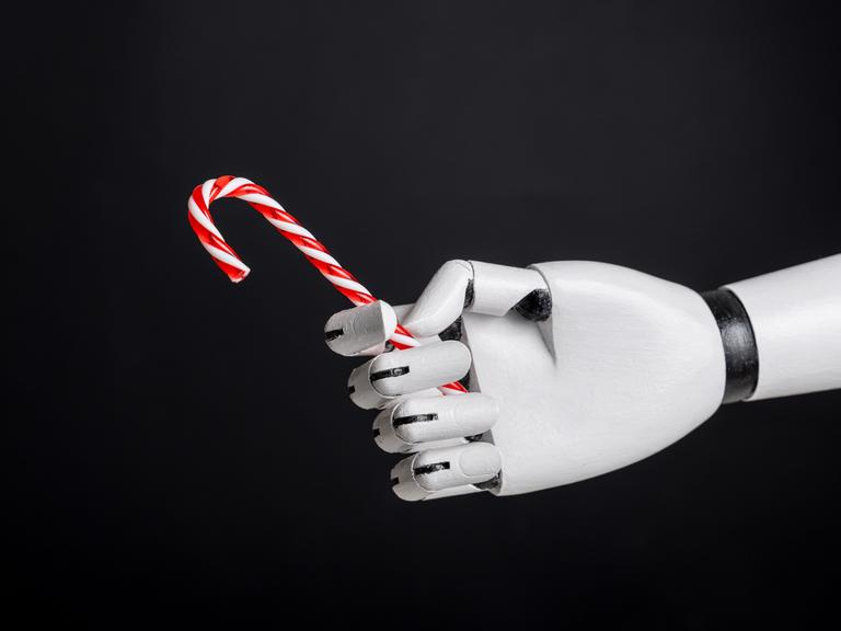Eine Roboterhand hält Zuckerstange vor schwarzem Hintergrund. 