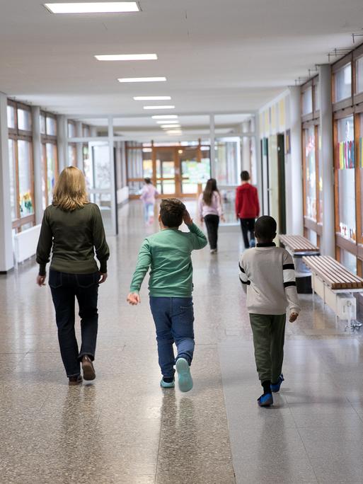 Schulkinder laufen mit einer Lehrerin einen Flur entlang
