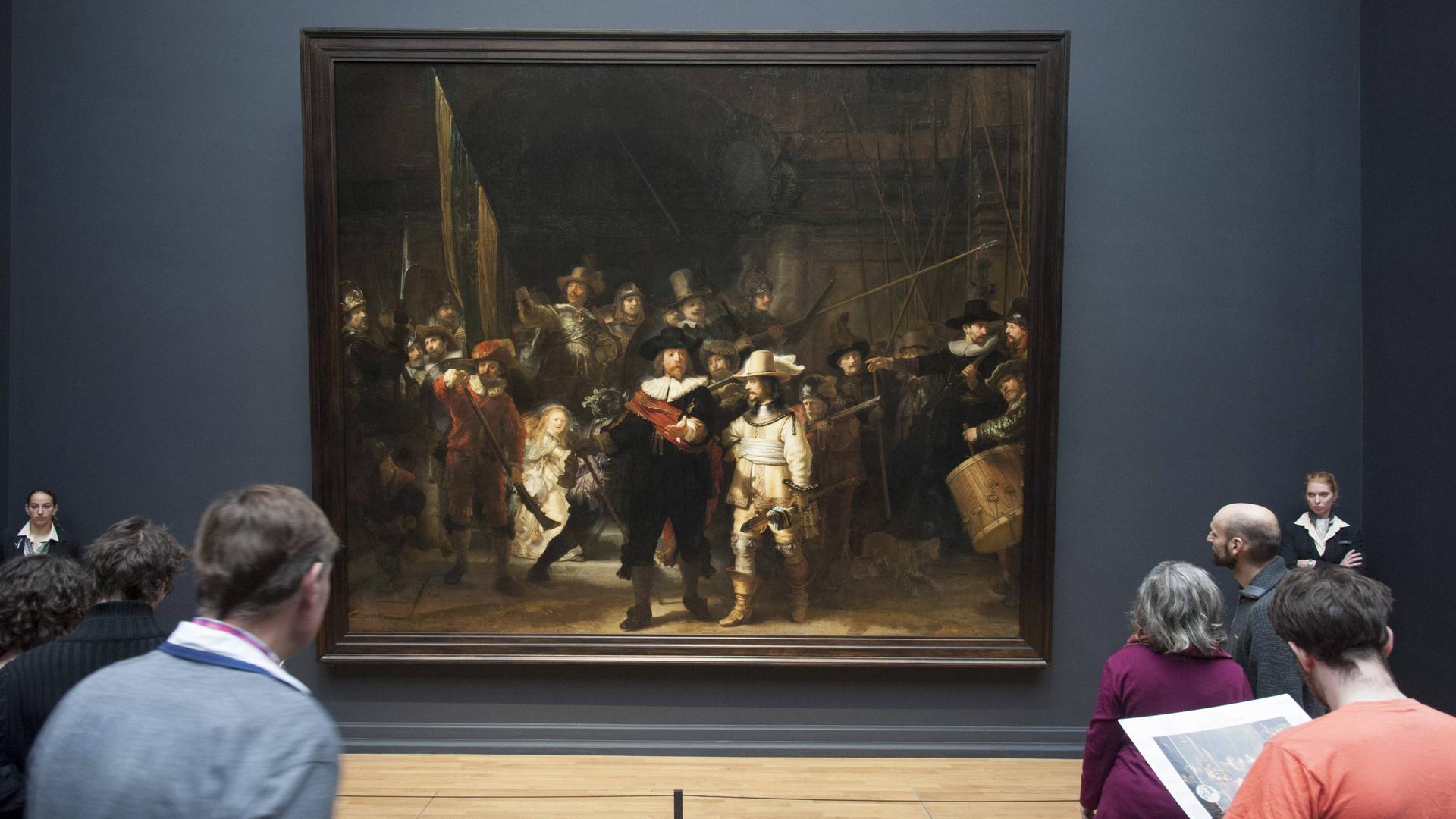 Besucher stehen im Rijksmuseum Amsterdam vor dem von zwei Museumswächtern bewachten Gemälde "Die Nachtwache" von Rembrandt  