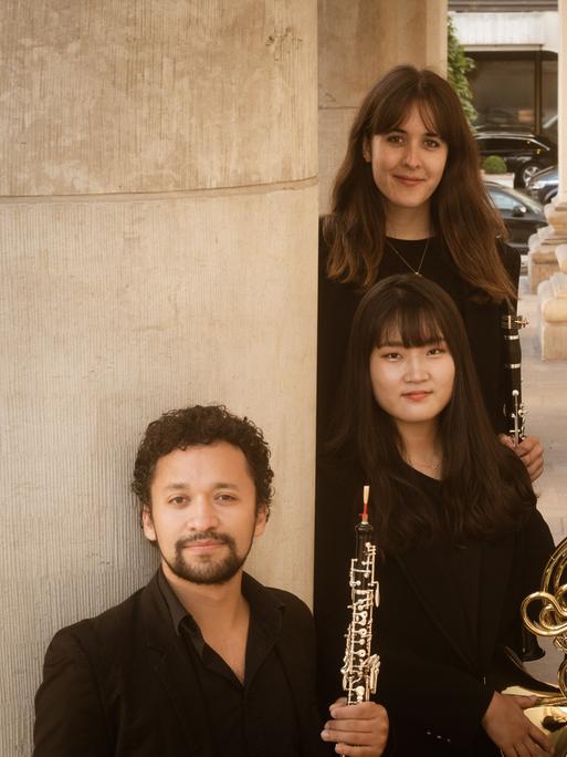 Zwei Musiker und drei Musikerinnen stehen mit ihren Instrumenten dicht beieinander in einer schmalen Straßenfront.