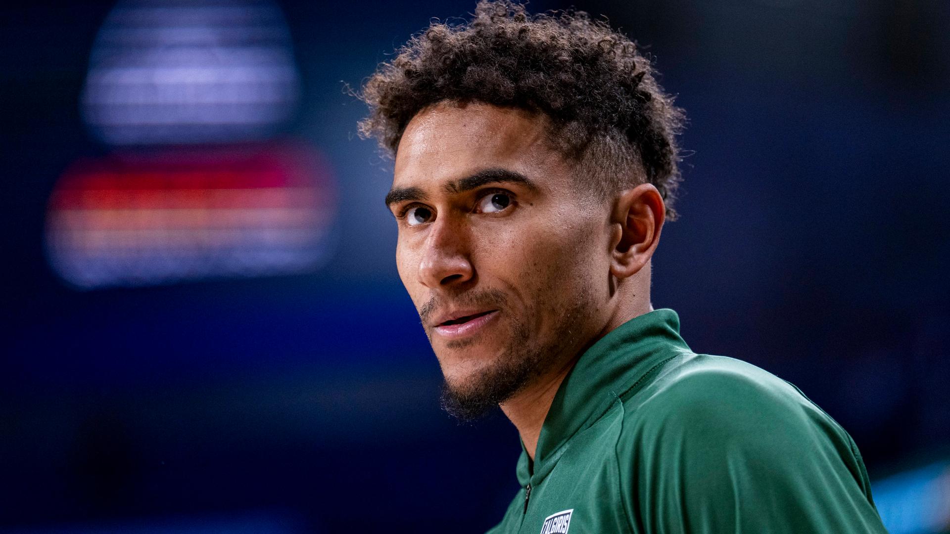 Ein Mann mit dunklen Locken und grünem Sportdress schaut ernst aus dem Bild hinaus. Ein Mann mit dunklen Locken und grünem Sportdress schaut ernst aus dem Bild hinaus.