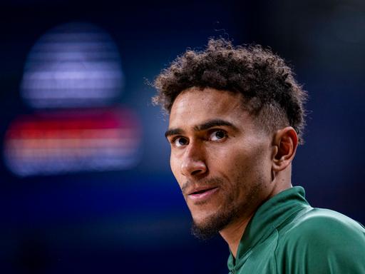 Ein Mann mit dunklen Locken und grünem Sportdress schaut ernst aus dem Bild hinaus. Ein Mann mit dunklen Locken und grünem Sportdress schaut ernst aus dem Bild hinaus.