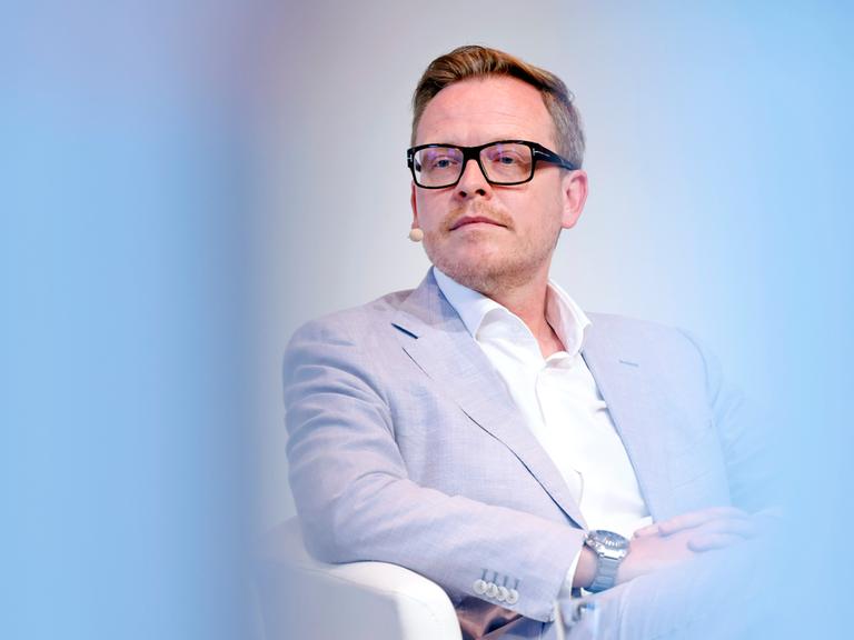 Porträt des Philosophen Markus Gabriel in einer Phil.Cologne Veranstaltung. Um ihn herum ist der Vordergrund hellblau verschwommen. Er trägt einen hellblauen Anzug und eine schwarze Brille.