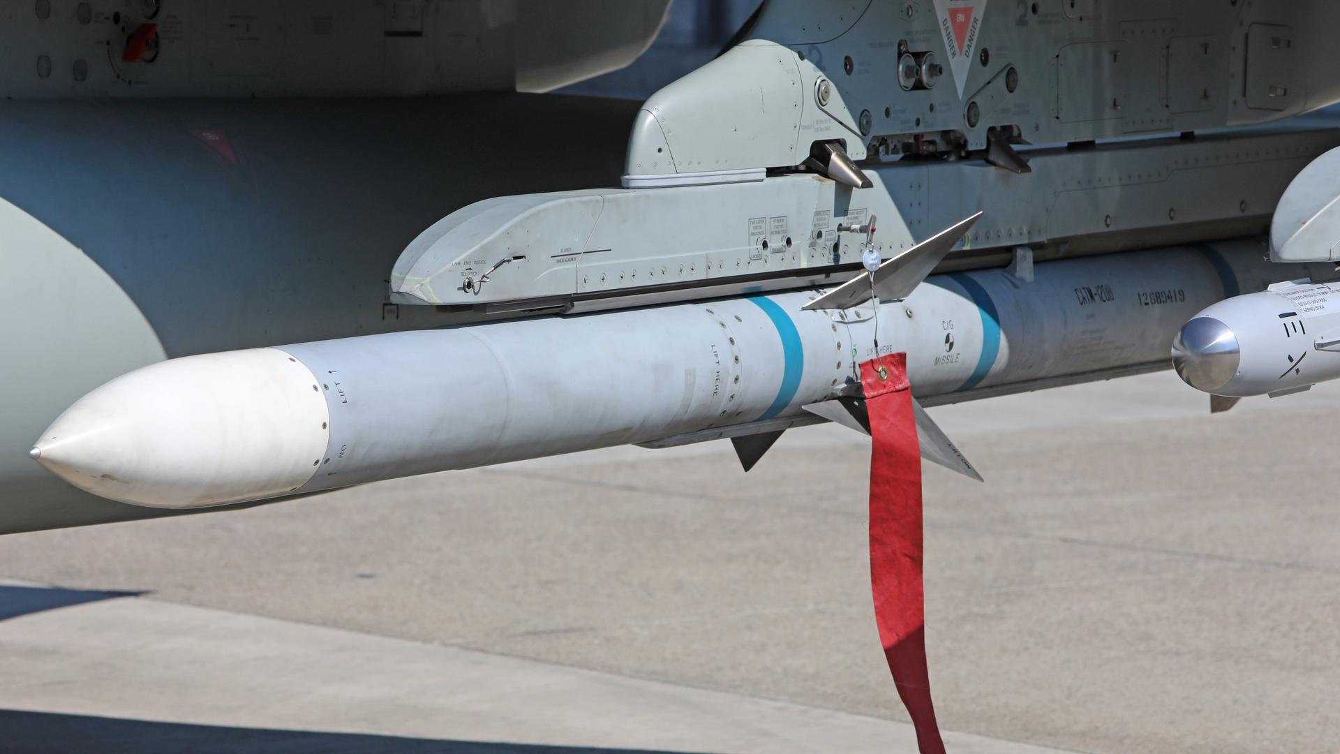 Näherer Blick auf die graue Rakete mit weißer Spitze, die an dem Flugzeug befestigt ist. An ihr hängt ein roter Wimpel.