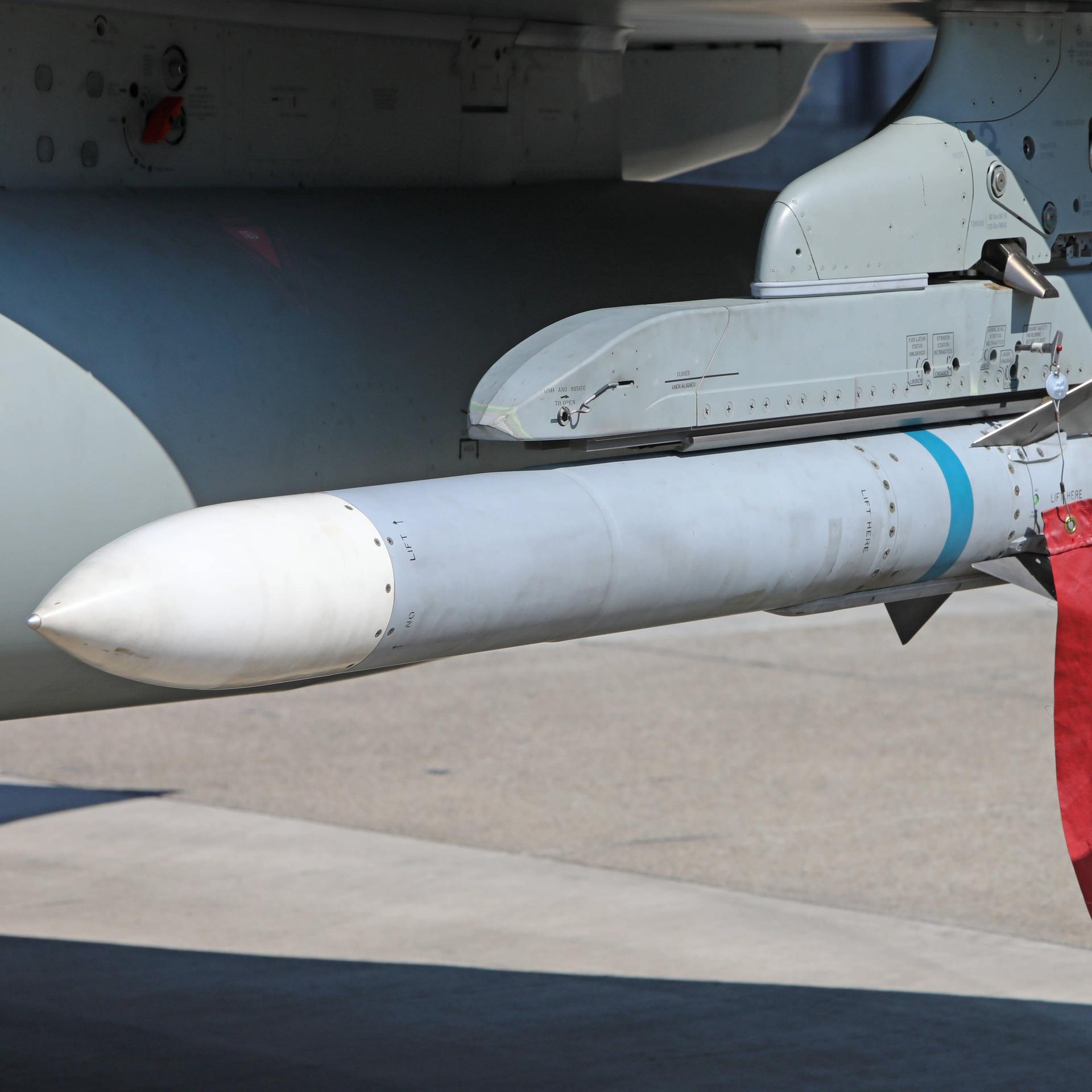 Näherer Blick auf die graue Rakete mit weißer Spitze, die an dem Flugzeug befestigt ist. An ihr hängt ein roter Wimpel.