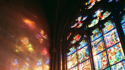 Licht scheint durch ein buntes Prager Kirchenfester und reflektiert farbig an der Wand