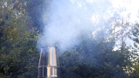 Rauchender Kamin eines Holzofens auf einem Dach.