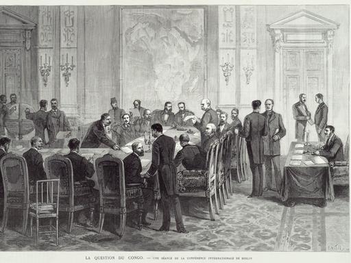 Eine Zeichnung aus 1884 zeigt die Kongokonferenz in Berlin; an einem Tisch sitzen Männer in Frack, weitere Männer stehen im Raum.