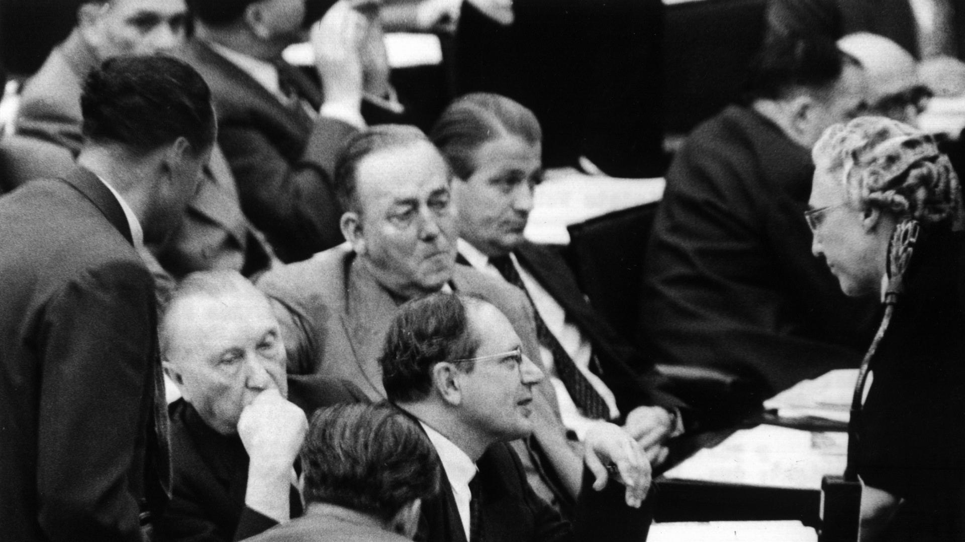 Auf dem Schwarz-weiß-Foto diskutiert eine ältere Frau mit mehreren Männern im Parlament des Deutschen Bundestags. 