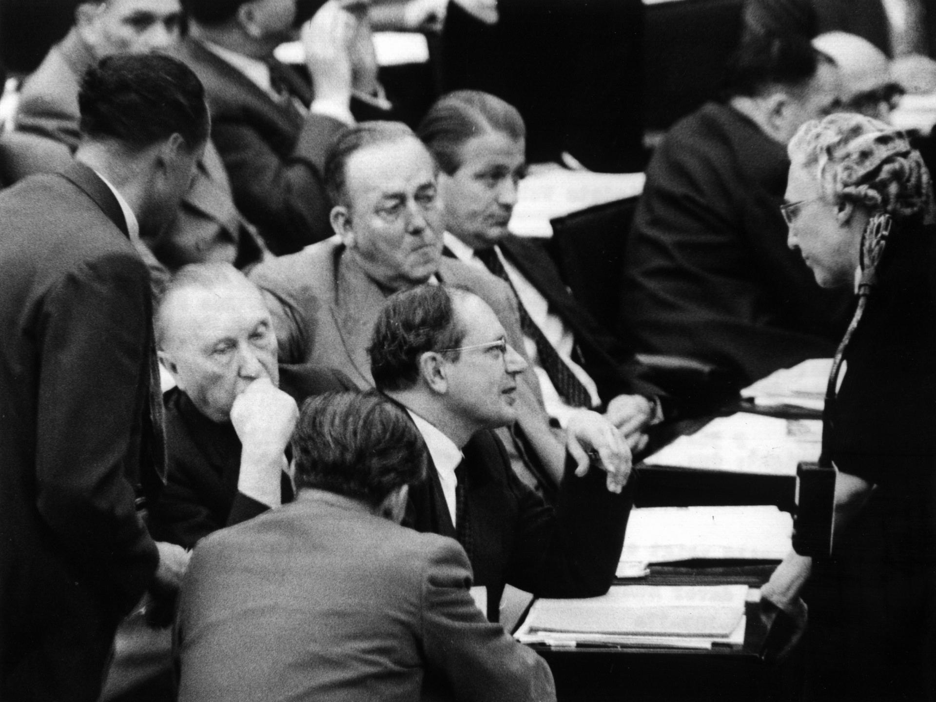 Auf dem Schwarz-weiß-Foto diskutiert eine ältere Frau mit mehreren Männern im Parlament des Deutschen Bundestags. 